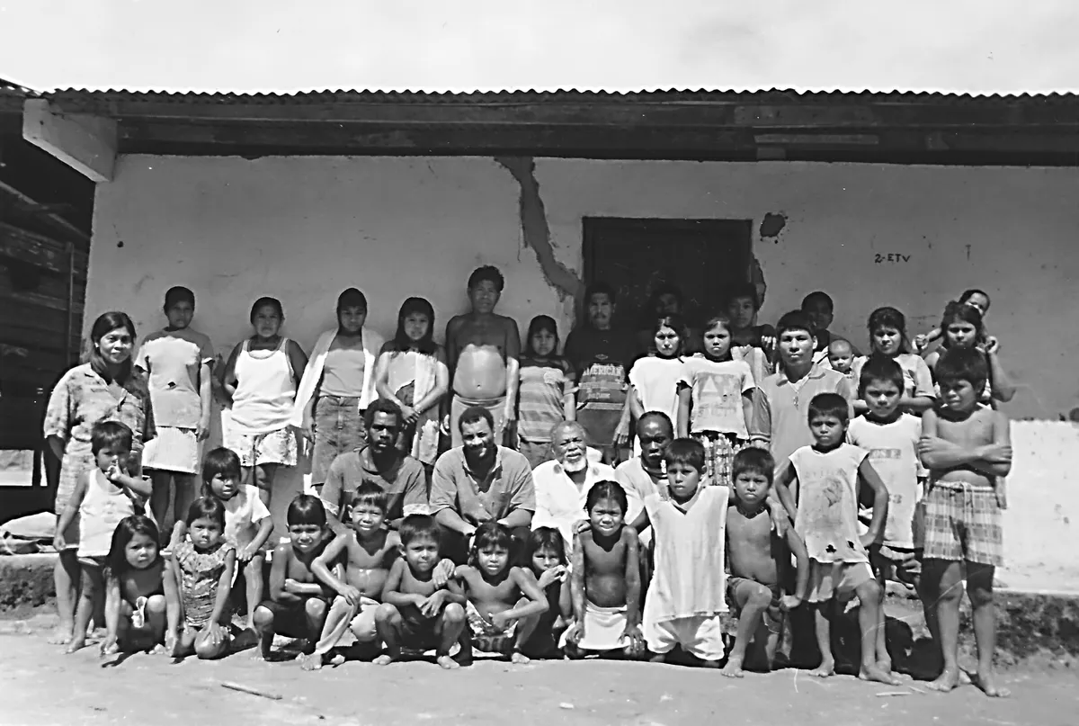 Arnoldo Palacios. Con la comunidad Emberá Katío, frente a una casa de tabla. Fotografía de Jota Palacios.